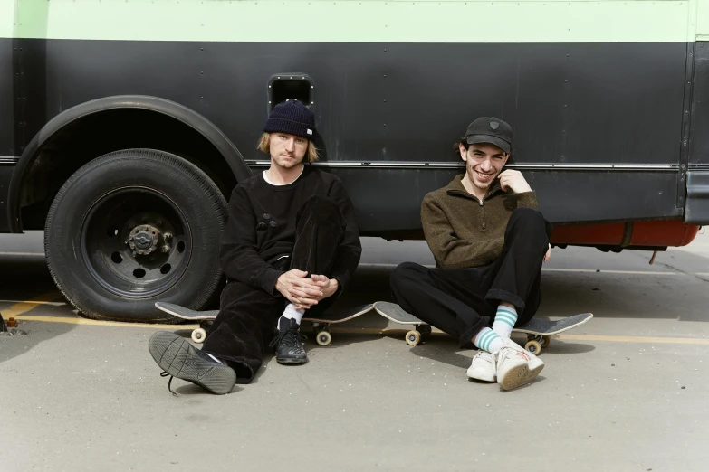 two men sitting on the ground next to a parked bus