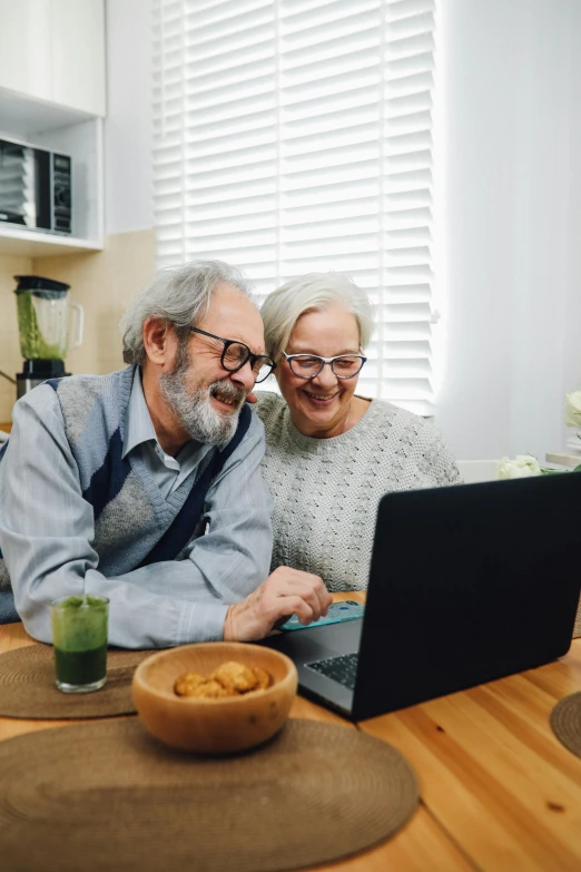 an older man and woman sitting on a chair looking at a laptop