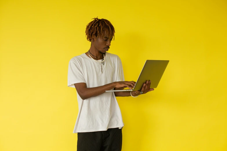 a young man using a laptop computer against a bright yellow background