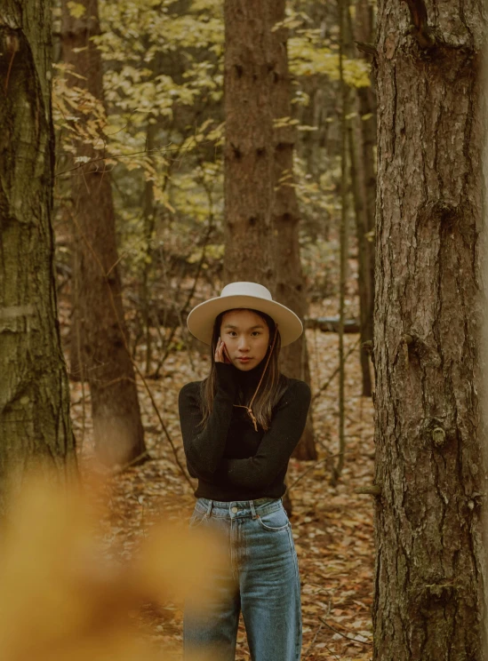 the young woman with hat stands in a wooded area