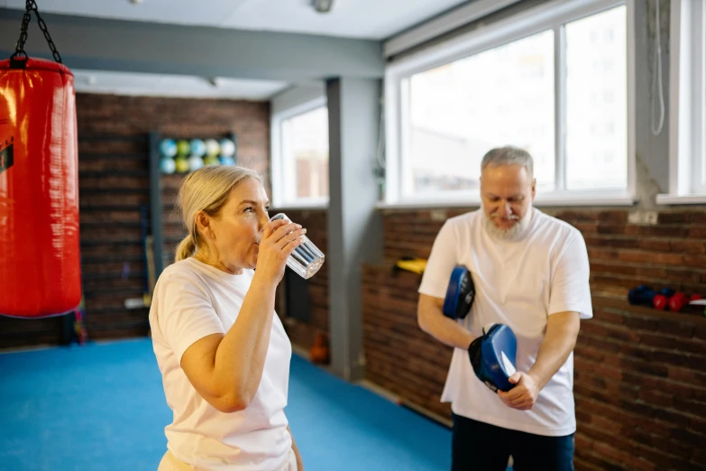 a woman drinking from a water bottle while holding a boxing glove