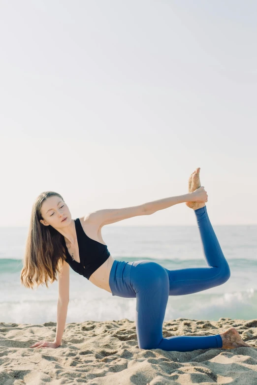 a woman in a sports  top doing yoga on the beach