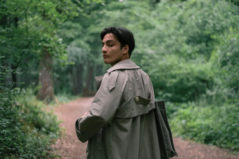 a man walking in the woods wearing a trench coat