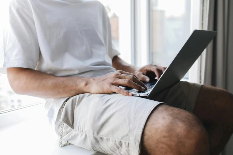 a man using a laptop on top of a window sill