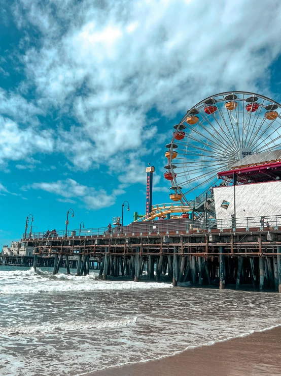 a ferris wheel next to the ocean with a cloudy blue sky