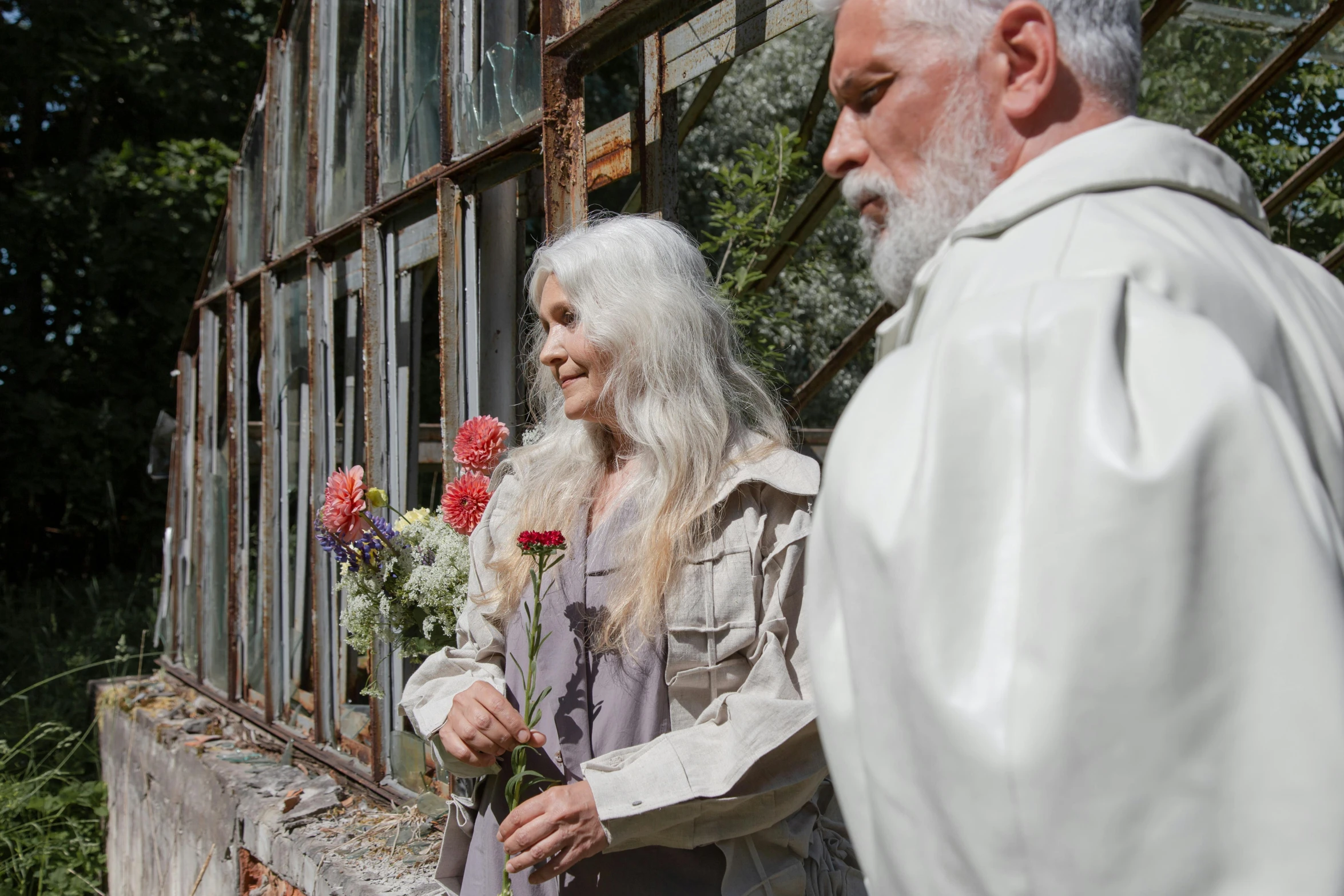 an elderly man and woman dressed in white flowers stand near a building