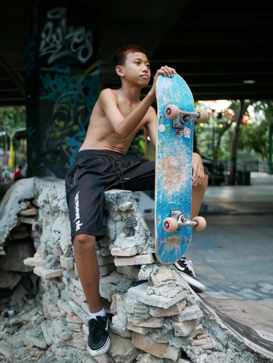 a young man holding a skateboard while sitting on a pile of rocks