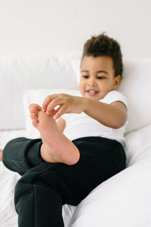 a boy sits on top of a bed as he puts his toes up