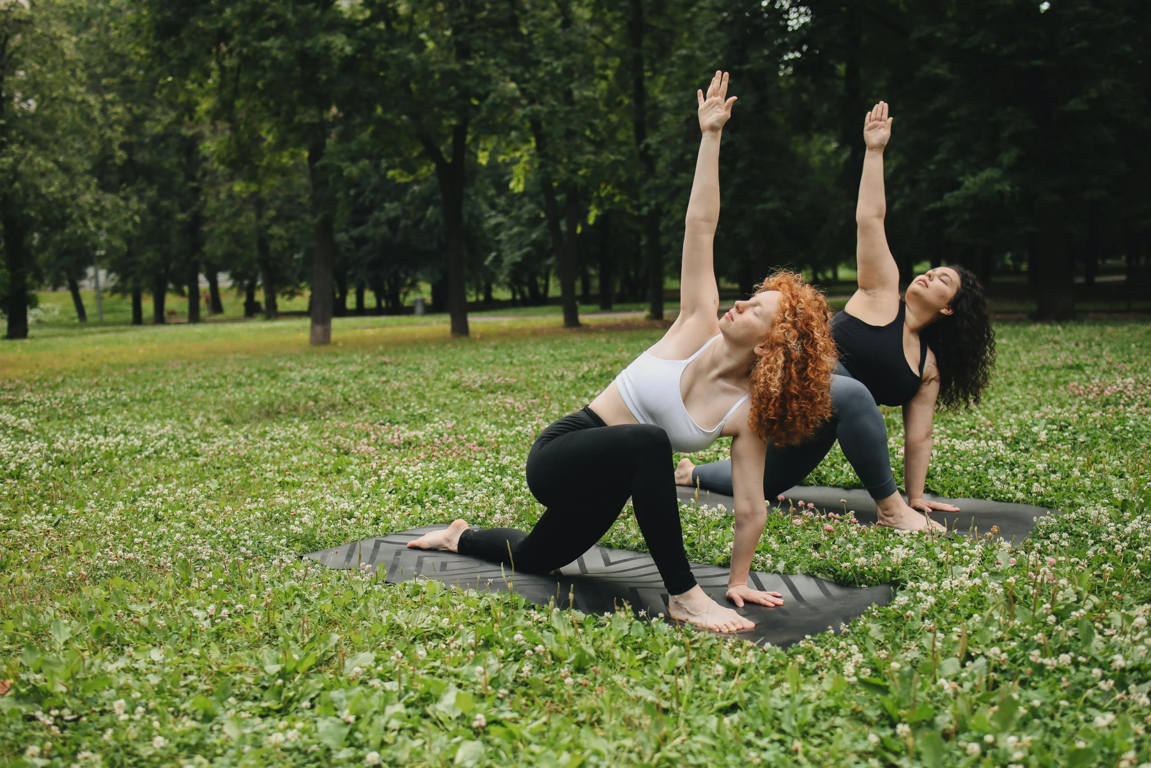 two women doing an exercise on a yoga mat in a park