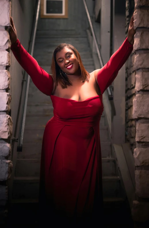 a woman in a red dress is standing next to a staircase