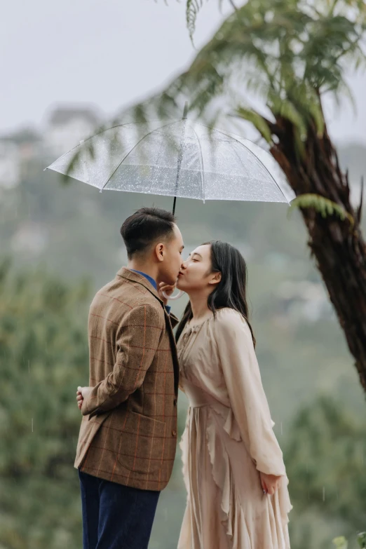 a couple sharing a kiss while standing in the rain under an umbrella