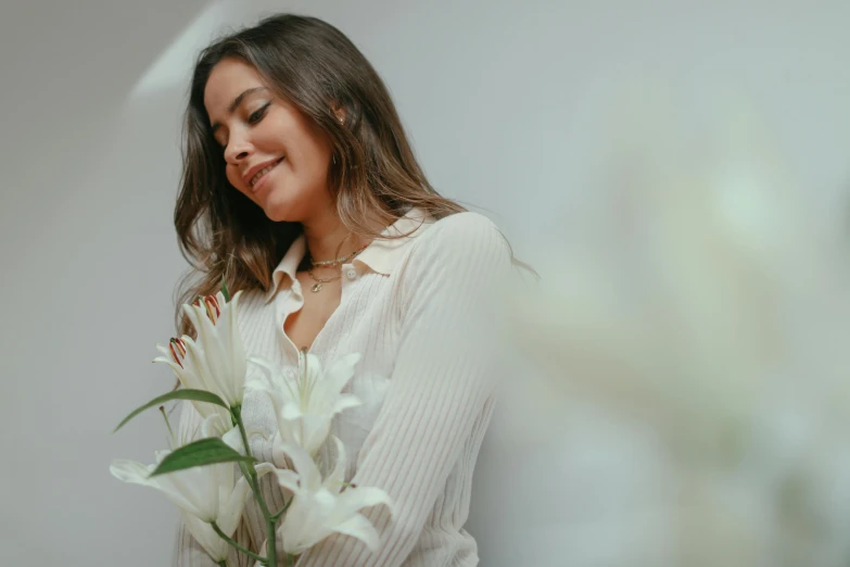 a woman in white sweater holding flower by the wall