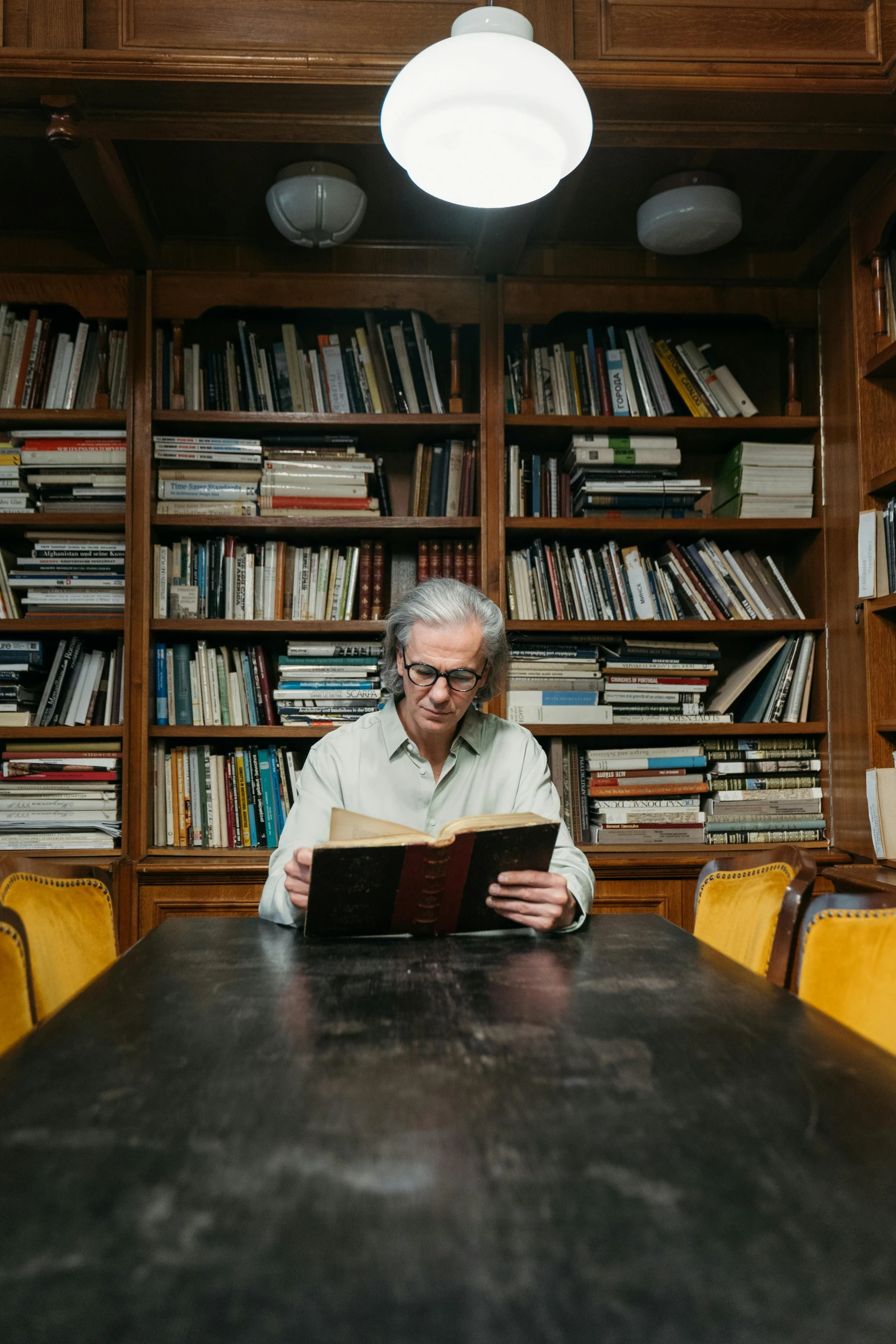 man sitting at table reading book in large liry