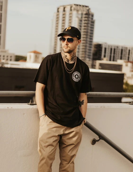 man in black t - shirt and tan pants stands next to wall