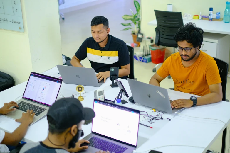 there are three men sitting at the desk working on their laptops