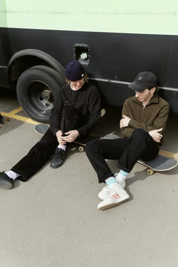 two men sitting on a parking lot with a bus behind them