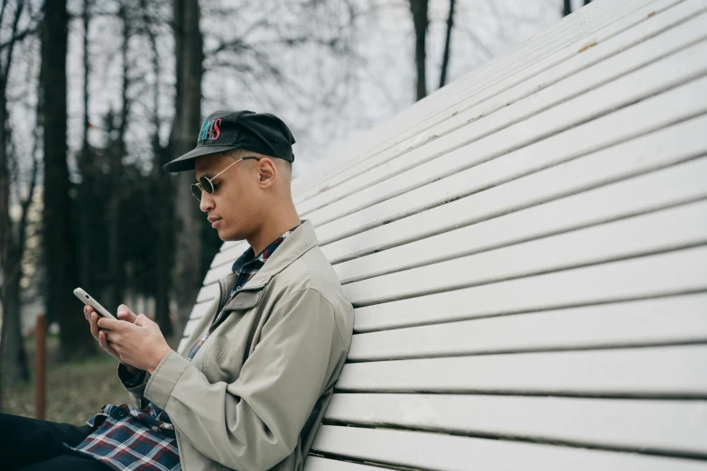 a man leaning up against a white bench while holding a cellphone