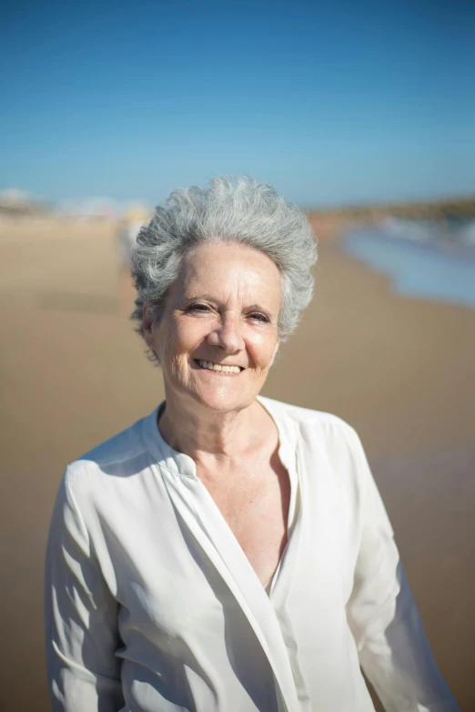 an elderly woman wearing white stands on the beach