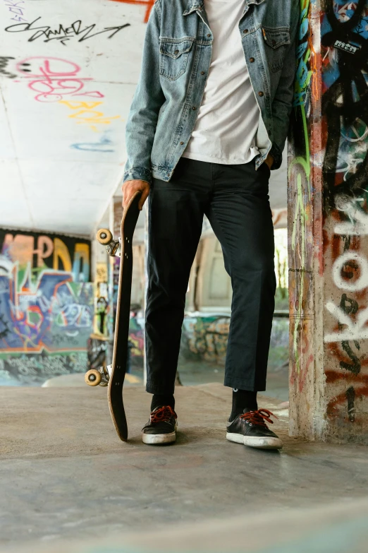 a man holding a skateboard next to a wall full of graffiti