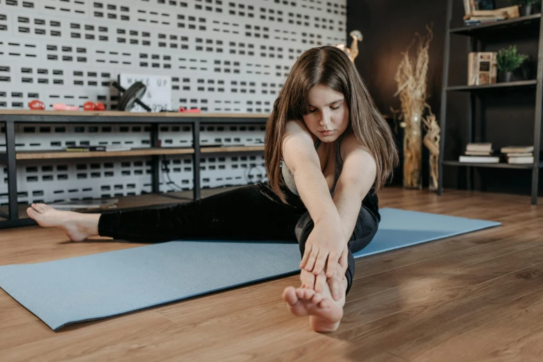  sitting on yoga mat in living room doing a back stretch