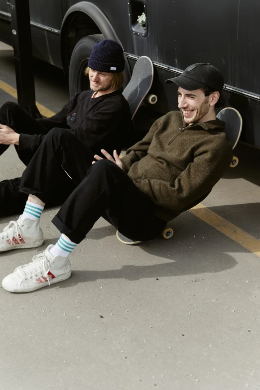 a pair of men sit on the ground near a skateboard