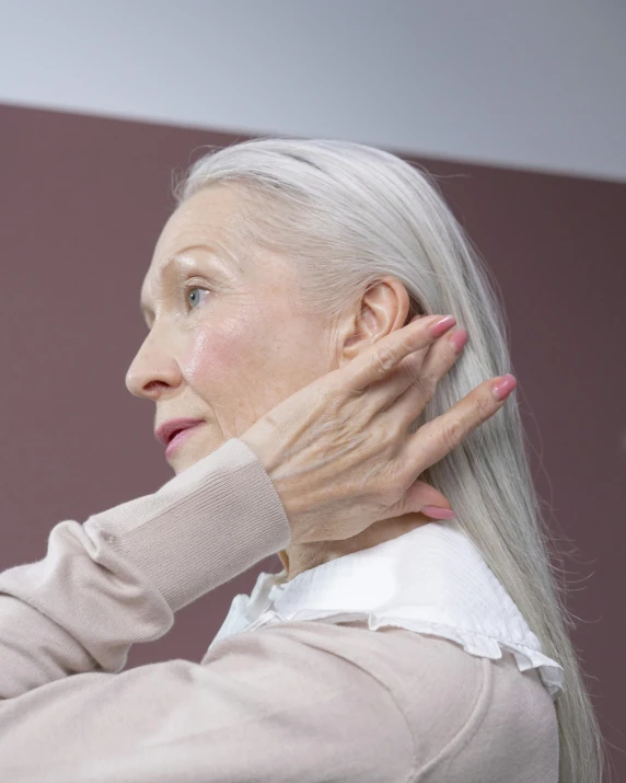 older woman with hand on neck standing in front of mirror