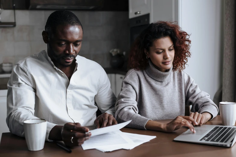 two people sitting at a table looking at a book and computer