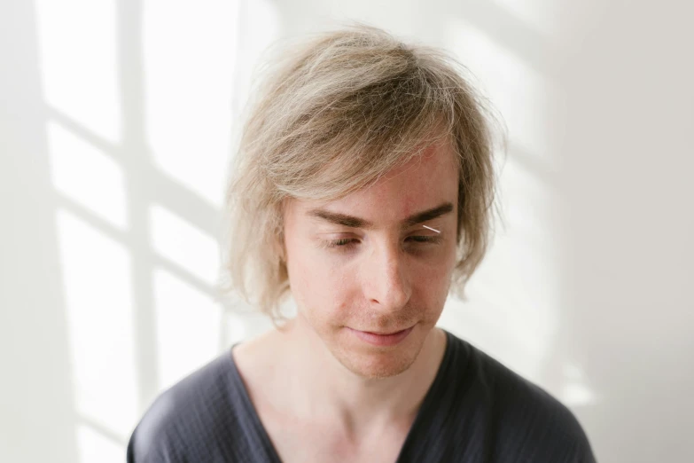 a young man with blonde hair wearing a cardigan shirt looking down