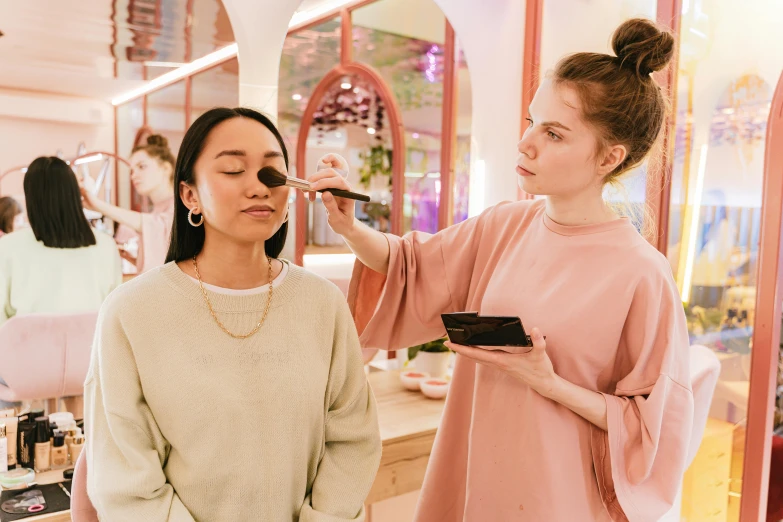 a woman looks into a mirror while her make - up artist works on her makeup