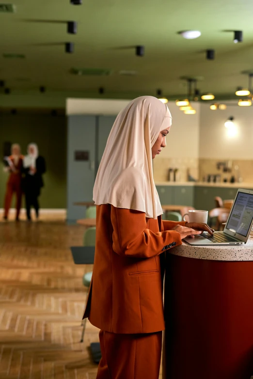 a woman in orange wearing a headscarf working on a laptop