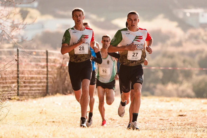 three men running in a field wearing cross country clothing