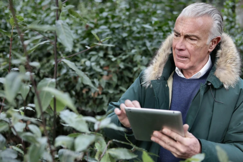 a man using a tablet while wearing a green jacket