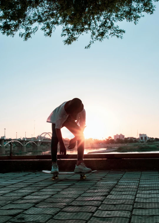a person bent over on a skateboard, standing in the sun