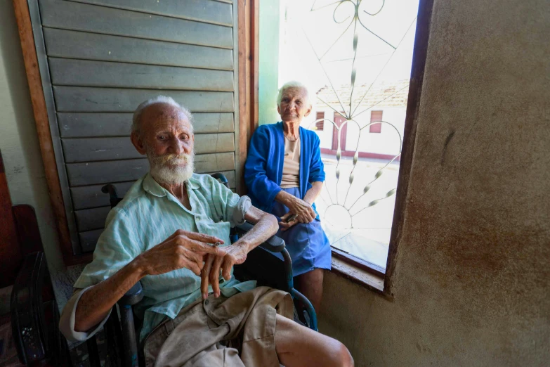 an elderly man sits in a wheel chair as he holds up his shirt