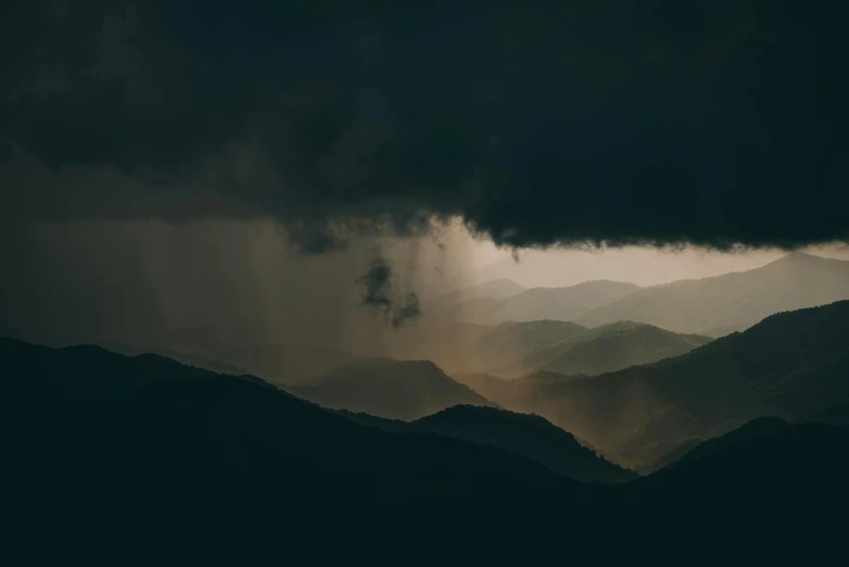 dark cloud over some mountains with a black sky