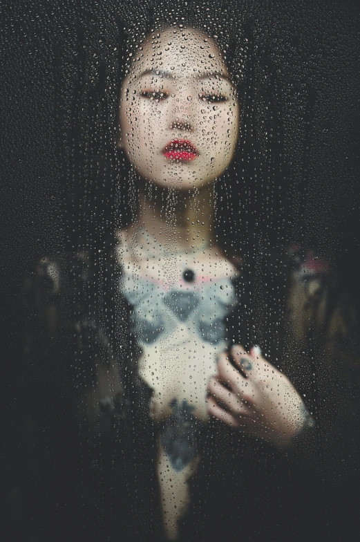 a woman looking out a window with rain coming on her