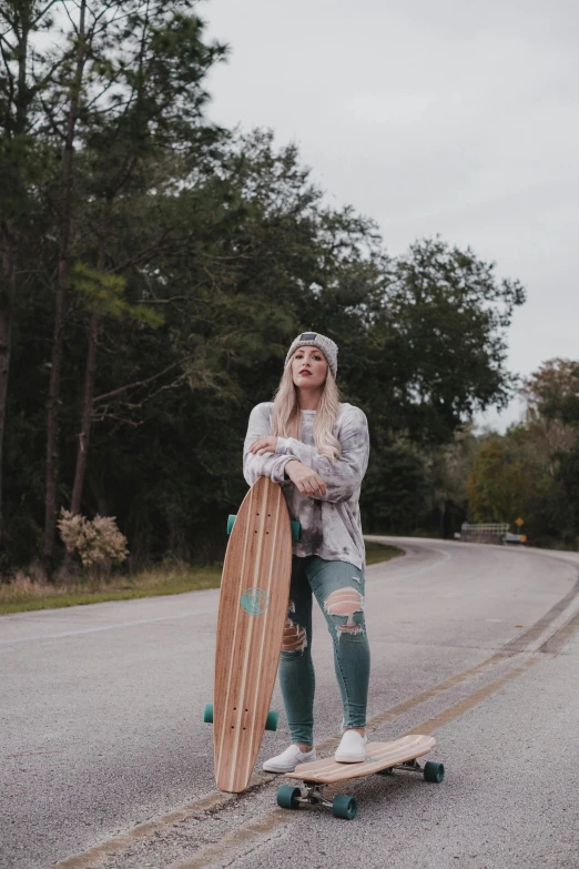 a young woman standing next to a skateboard on the road