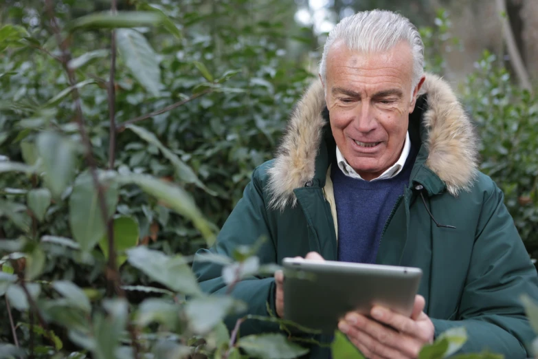 the old man is looking at the tablet in the forest