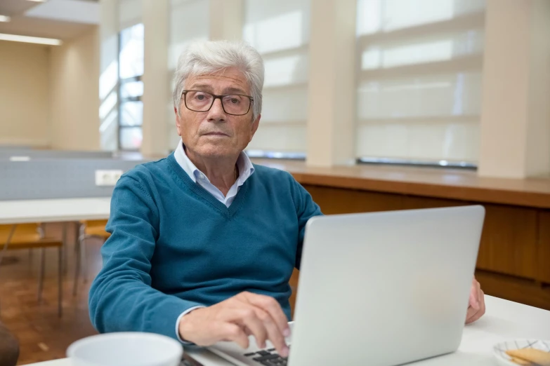 an old man with glasses works on a laptop