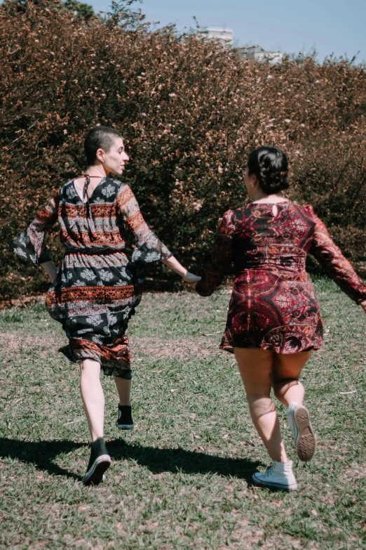 two women in dresses walking down a grassy field