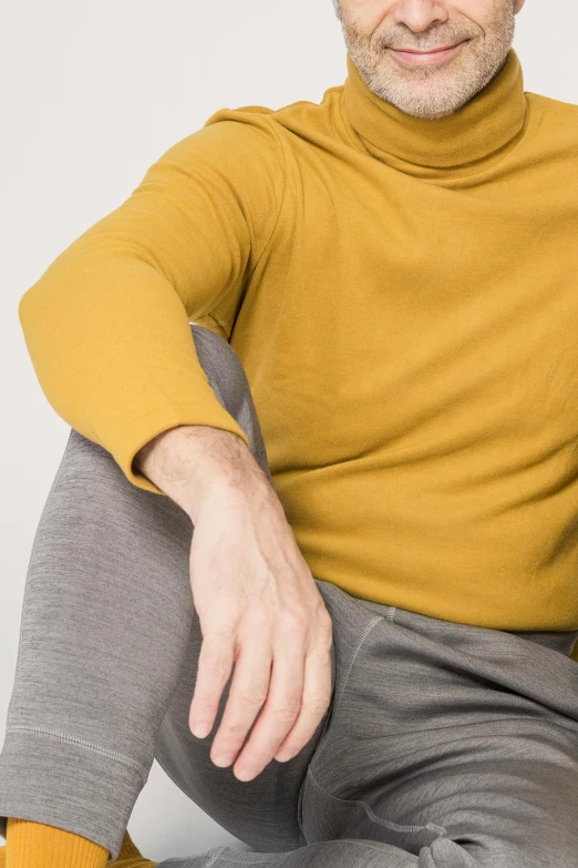 a man in a mustard shirt and gray pants with his legs crossed