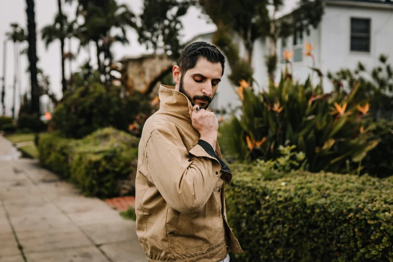 man in tan jacket walking on sidewalk talking on cell phone