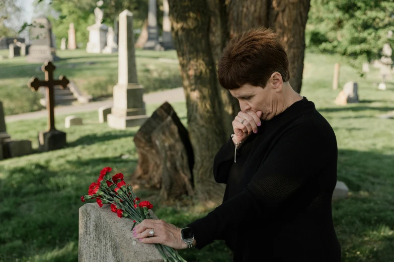 a woman wiping her face while placing flowers on a cemetery wall