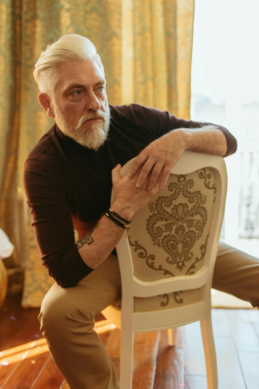 a bearded man leaning on a white chair