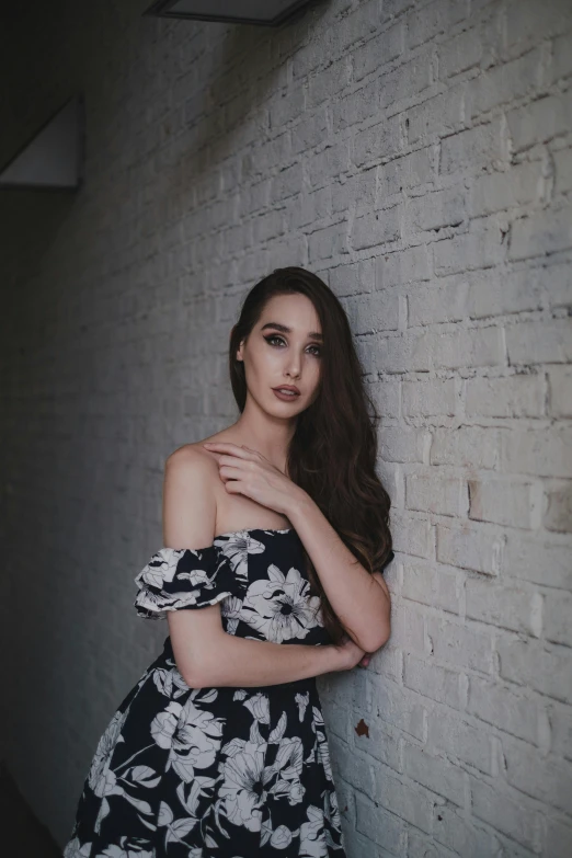 a woman leans against a brick wall with her hand on her chest