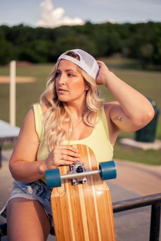 a girl in a yellow tank top is sitting holding a wooden skateboard