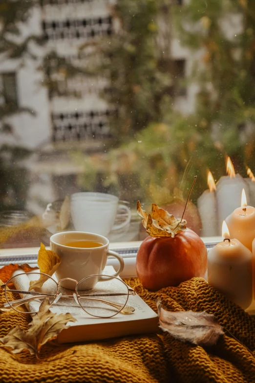 the view of candles, a book and a cup sit on a blanket