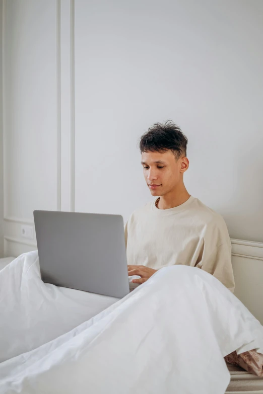 a boy in white shirt on a laptop sitting on bed