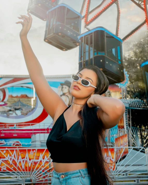 a girl wearing sunglasses waving up while standing by an amut ride