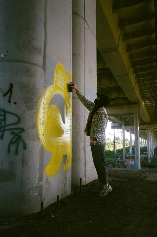 a man is reaching up to paint a yellow mural on a cement wall